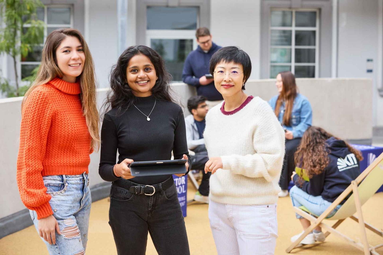 Drei Studenten auf dem Campus blicken nach oben, während sie gemeinsam ein iPad halten. Die Szene vermittelt Teamwork, Lernen und moderne Technologie in der Hochschulbildung.