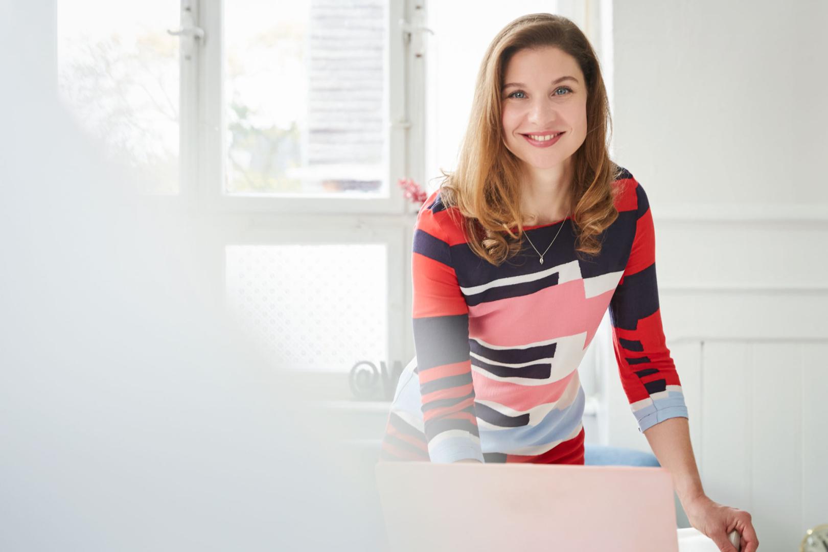 Professionelles Personal Branding: Eine Frau lehnt vor ihrem Computer und blickt selbstbewusst in die Kamera. Der unscharfe Vordergrund sorgt für eine moderne und fokussierte Bildästhetik.